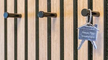 A set of keys with a label 'Haus Pop Inselstern' hanging on a wooden wall with vertical slats.