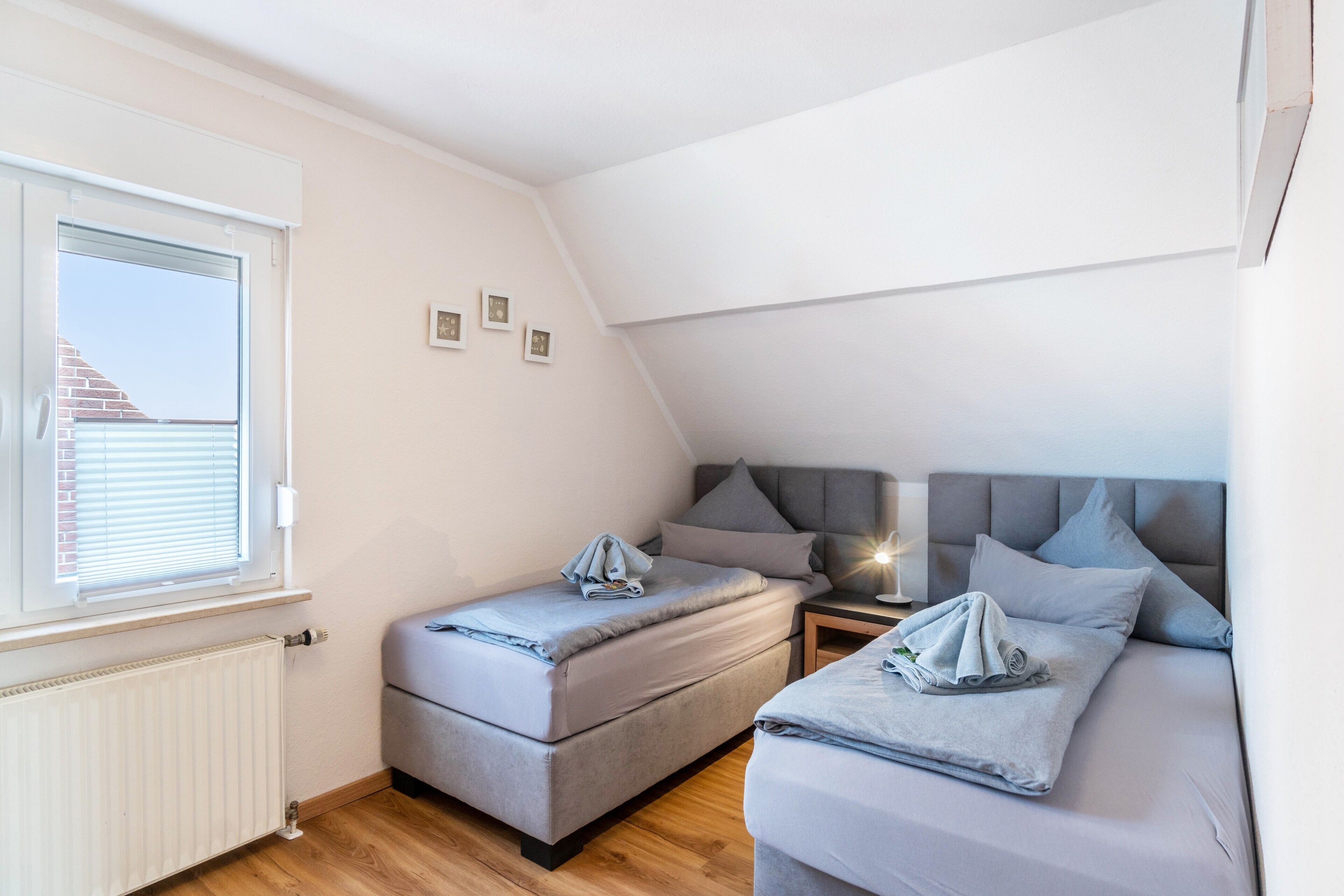 Une chambre avec deux lits, une fenêtre, un radiateur et une table de chevet avec une lampe.