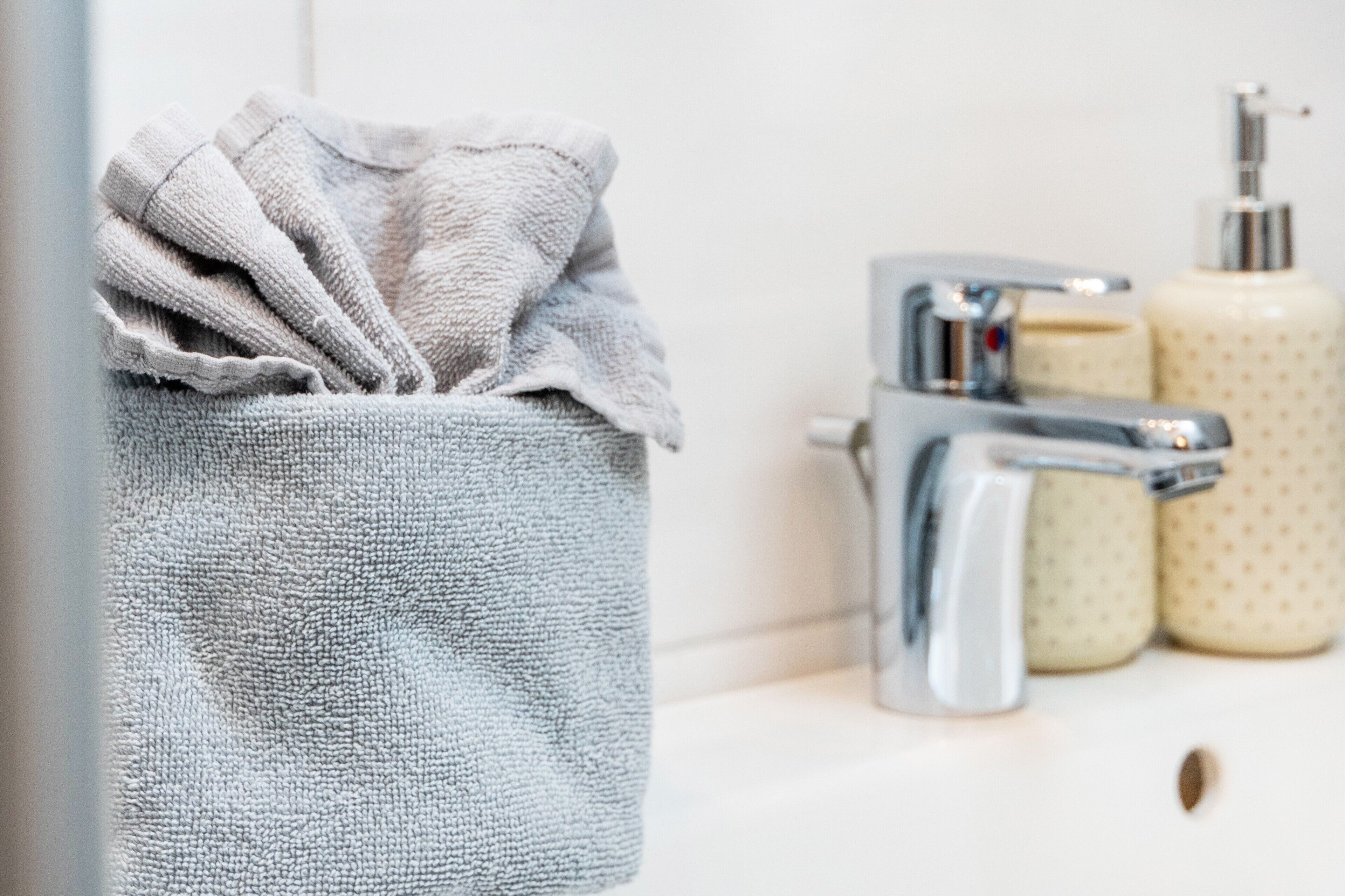 A bathroom with a towel hanging on a rack, a faucet, and two soap dispensers.
