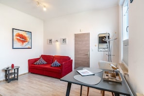 Un salon moderne avec un canapé rouge, une petite table, une œuvre d’art encadrée et un porte-manteau.