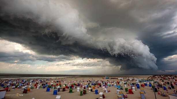 A beach with numerous colorful beach umbrellas and chairs, a vast sky with dark clouds, and a calm sea. - Holiday Home 'Südstrand' on Borkum for 2–4 Guests, 2 Bedrooms (Borkum)