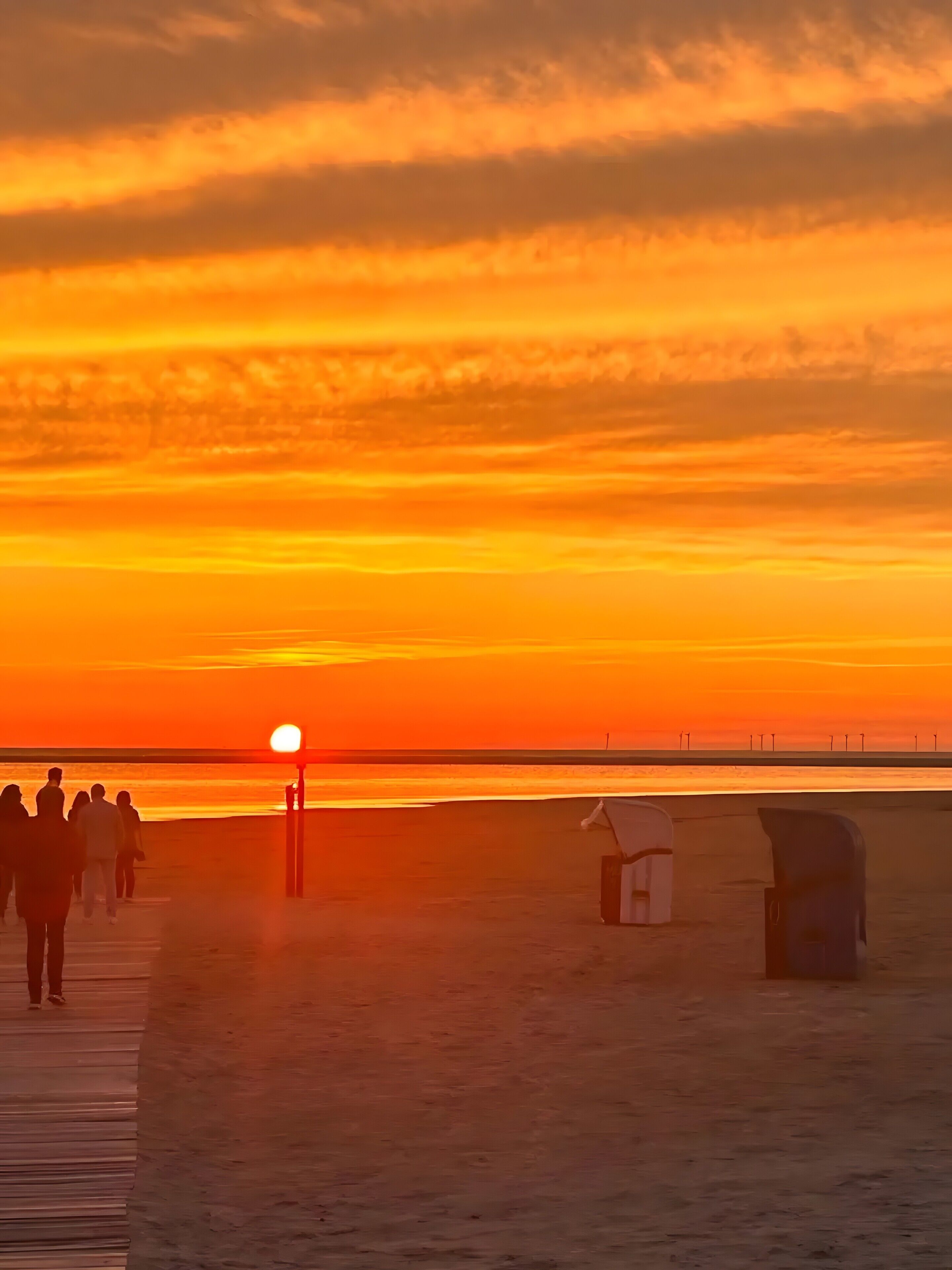 A sunset over a beach with a wooden walkway and a small structure.