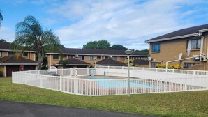 A residential area with a swimming pool surrounded by a white fence, houses with brick exteriors, and a clear blue sky. - 5 Beach Dunes (Richards Bay)
