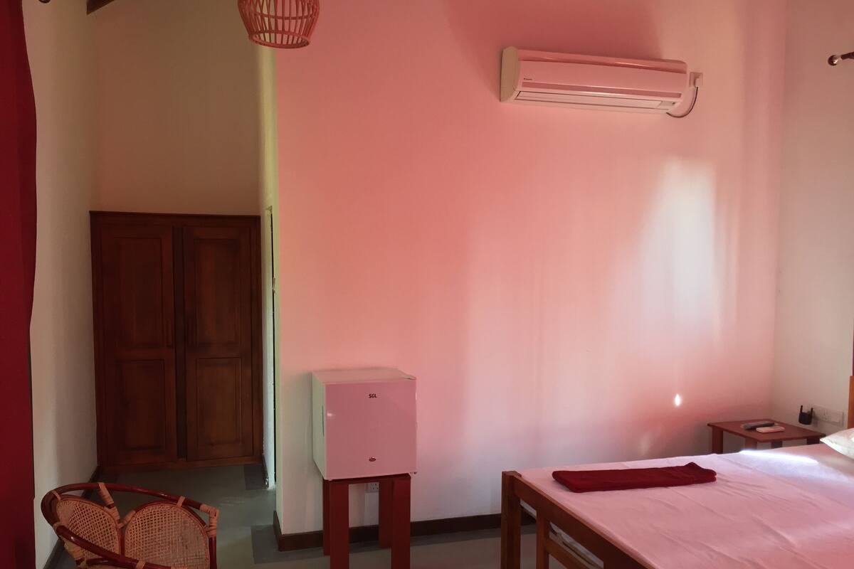 Quarto com cama, mesa pequena, cadeira, ar condicionado e guarda-roupa.