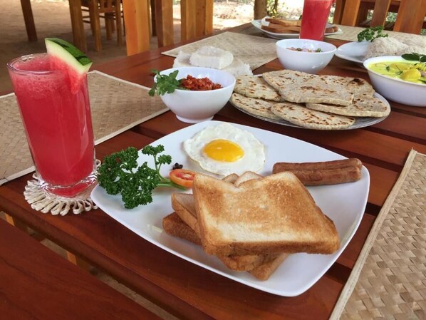 A breakfast plate with toast, fried egg, sausage, and a glass of red drink.