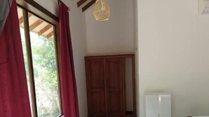 A room with a large window, wooden wardrobe, a small table, and a hanging light fixture.