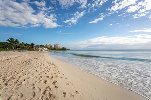 Ein Strand mit Fußabdrücken, Palmen und Gebäuden im Hintergrund.