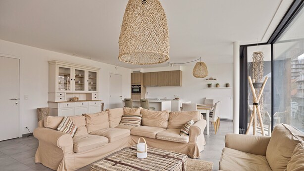 A modern living room with a beige sofa, a wicker coffee table, and a large window with a view of the city. - The Green 15 0301 met garage (Nieuwpoort)