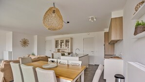 A modern kitchen with white cabinets, a wooden dining table, and a hanging woven light fixture. - The Green 15 0301 met garage (Nieuwpoort)