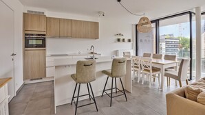 A modern kitchen with wooden cabinets, a built-in oven, and a dining area with a white table and chairs. - The Green 15 0301 met garage (Nieuwpoort)