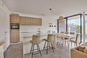 Eine moderne Küche mit Holzausstattung, einem Einbauofen und einem Essbereich mit weißem Tisch und Stühlen.