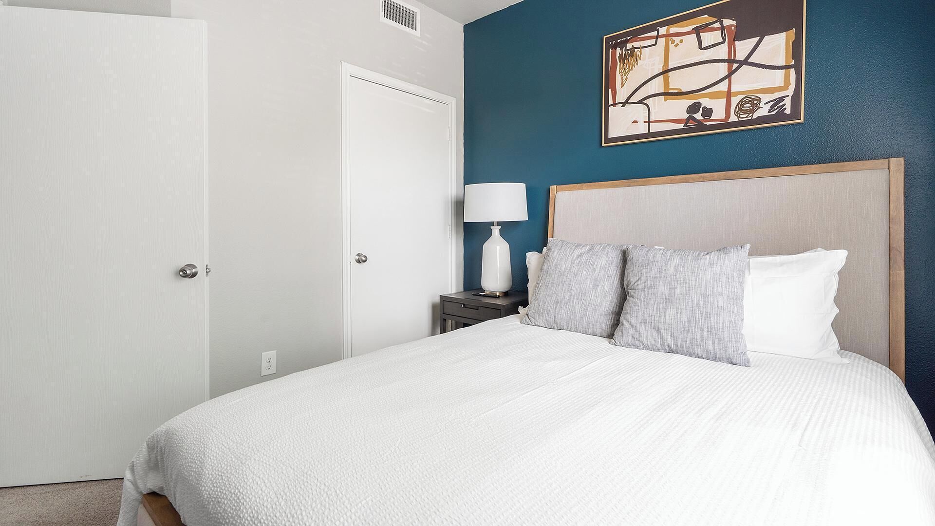 A hotel room with a large bed, a nightstand with a lamp, and a painting on the wall.