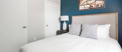 A hotel room with a large bed, a nightstand with a lamp, and a painting on the wall.