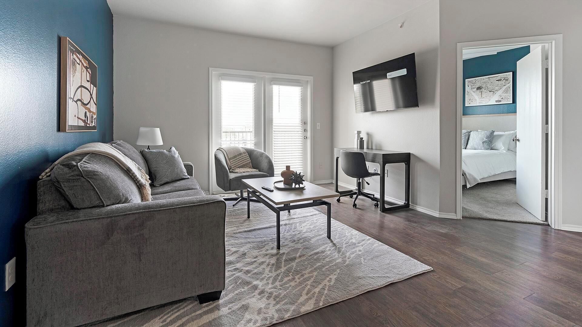 A modern living room with a gray sofa, a coffee table, and a TV on the wall.