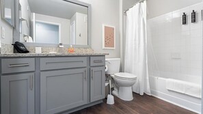 A modern bathroom with a grey vanity, white toilet, and a shower area. - Landing Furnished Apartments - Far West Side (San Antonio)