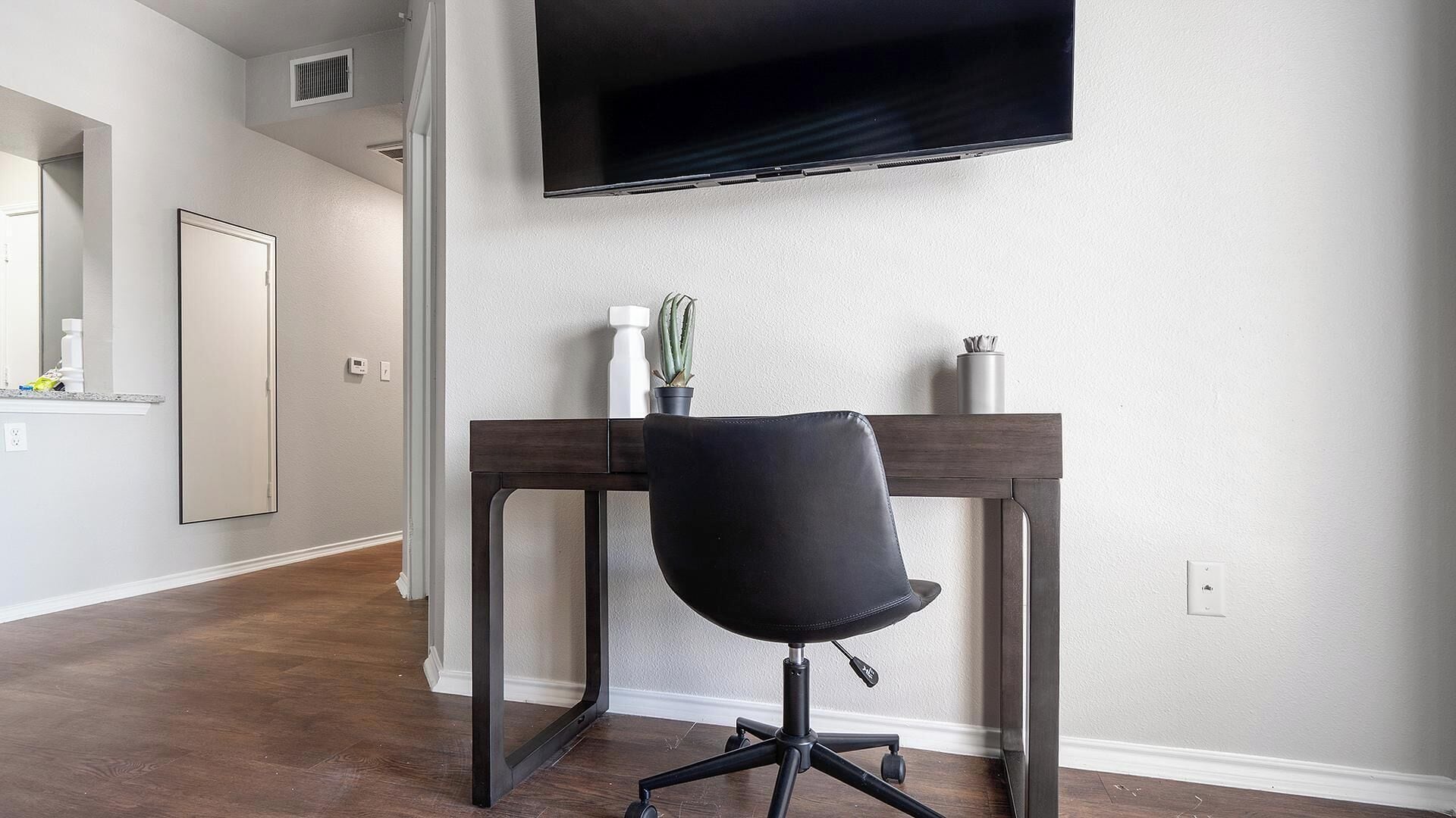 A modern office space with a desk, chair, and a mounted flat-screen TV.