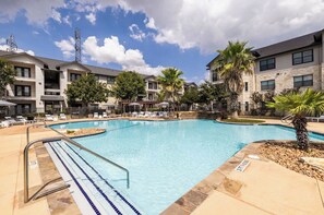 A swimming pool with a clear blue water, surrounded by lounge chairs and palm trees. - Landing Furnished Apartments - Far West Side (San Antonio)