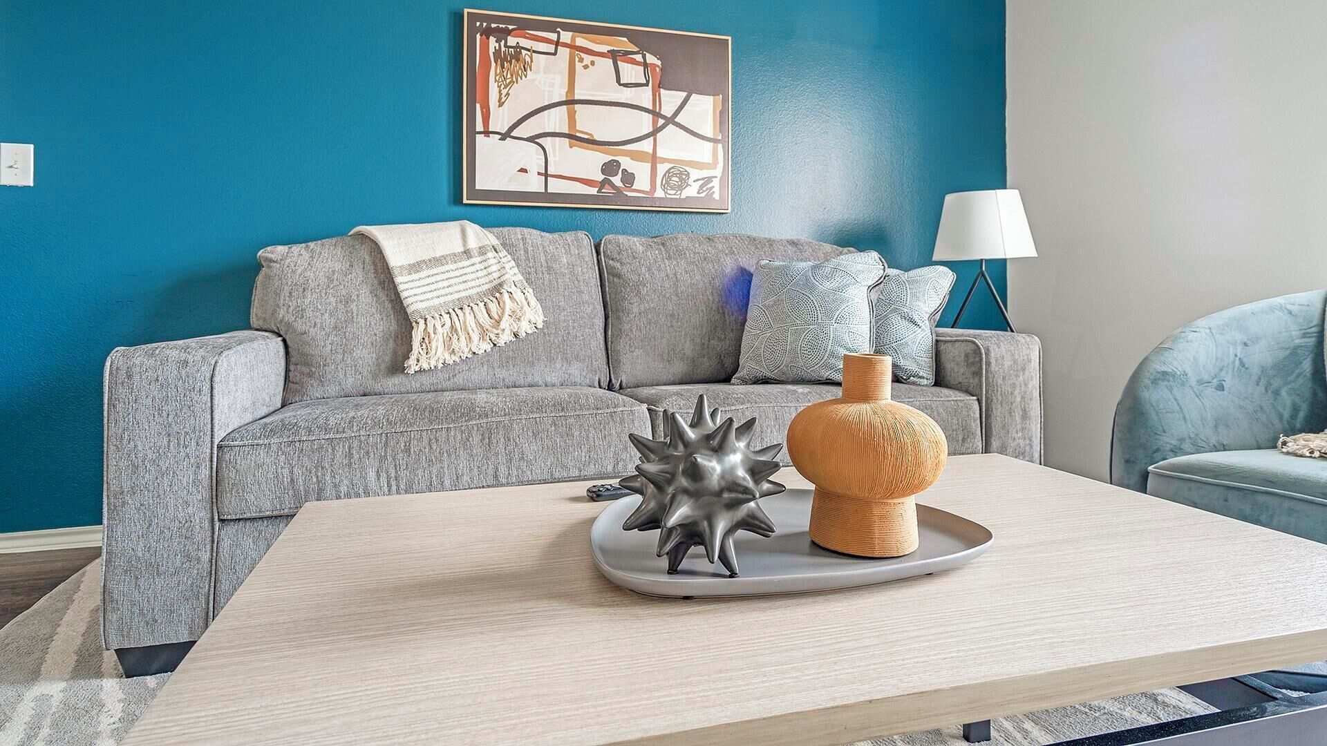 A modern living room with a grey sofa, a coffee table with decorative items, and a blue accent wall.
