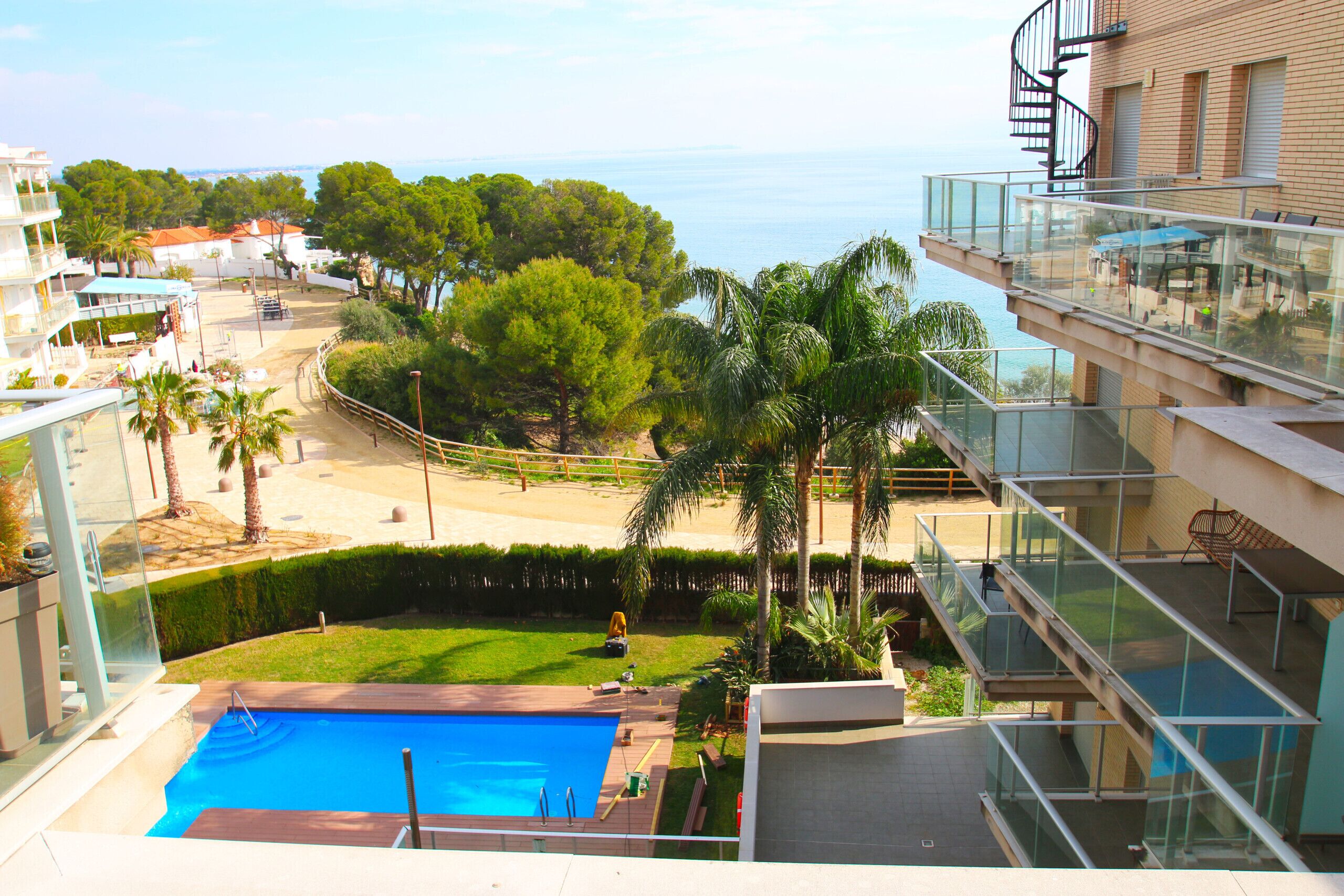 Piscina com vista para o mar, rodeada por palmeiras e um espaço gramado.