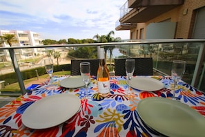 A balcony table set with plates, glasses, and a bottle of Clamour wine, overlooking a residential area with palm trees and buildings.