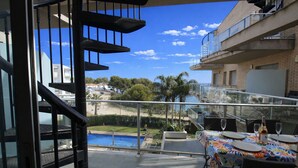 A balcony with a dining table set for two, overlooking a pool and a building with a balcony. - Apartment Panoramic 25 by Parc Mont-roig (Miami Playa)
