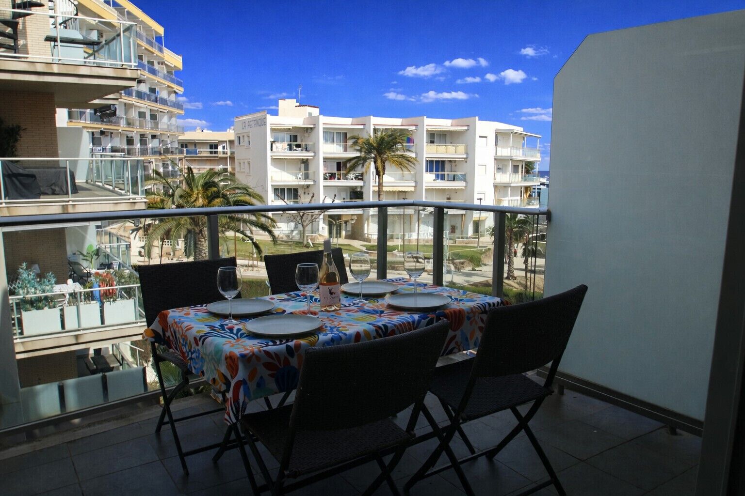 Un balcon avec une table dressée pour le dîner, donnant sur un quartier résidentiel avec de nombreux immeubles et des palmiers.