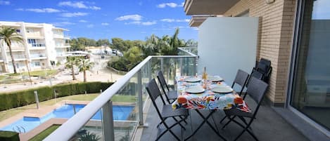 Un balcón con una mesa dispuesta para dos, con vistas a una piscina y una zona residencial.