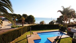 A swimming pool with a wooden deck, surrounded by well-maintained grass and palm trees, overlooking a body of water. - Apartment Panoramic 26 by Parc Mont-roig (Miami Playa)