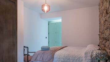 Un dormitorio con una cama, un armario de madera, una pared de piedra, una lámpara colgante y una puerta que da a otra habitación.