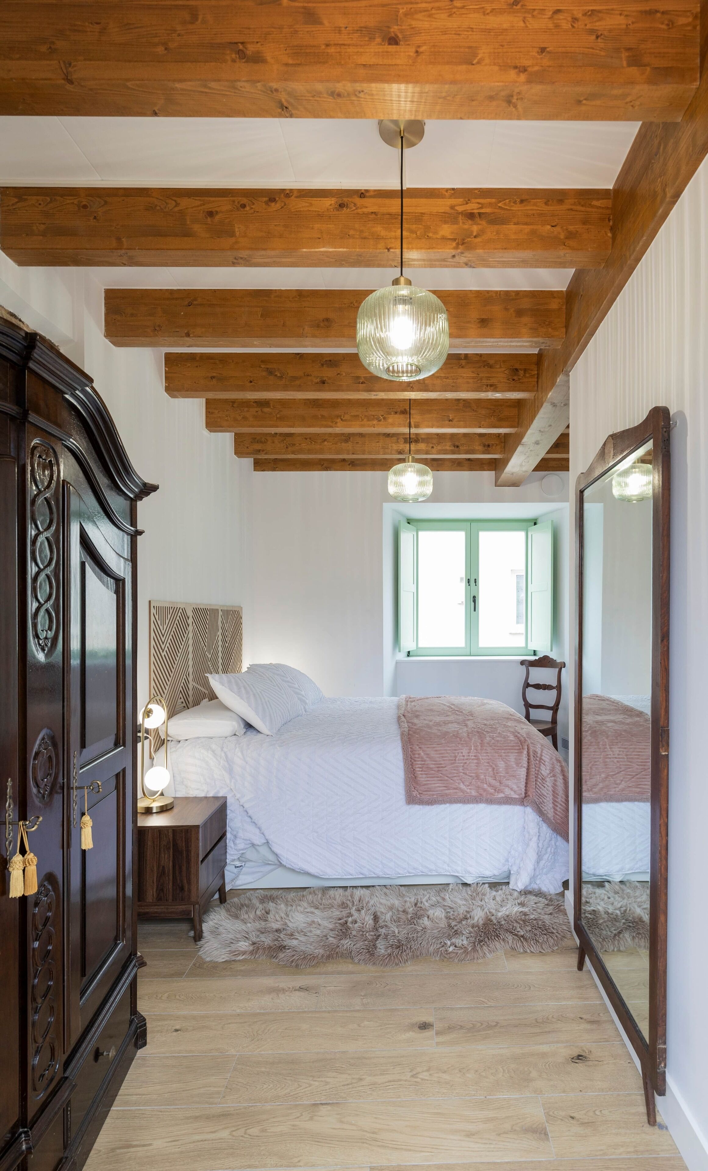 Een slaapkamer met een houten plafond, een groot bed, een nachtkastje, een spiegel en een raam.