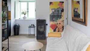 A cozy living room with a white sofa, a small round table, a black heater, and a window with green shutters. - El Sueño Parrita Peñaronda Beach (Castropol)