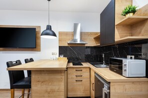 A modern kitchen with a wooden island, black countertop, stainless steel appliances, and a black pendant light. - Imperial Central Residences West (Rijeka)
