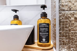 A bathroom with a white sink, two bottles of shampoo, and a textured wall. - Imperial Central Residences West (Rijeka)