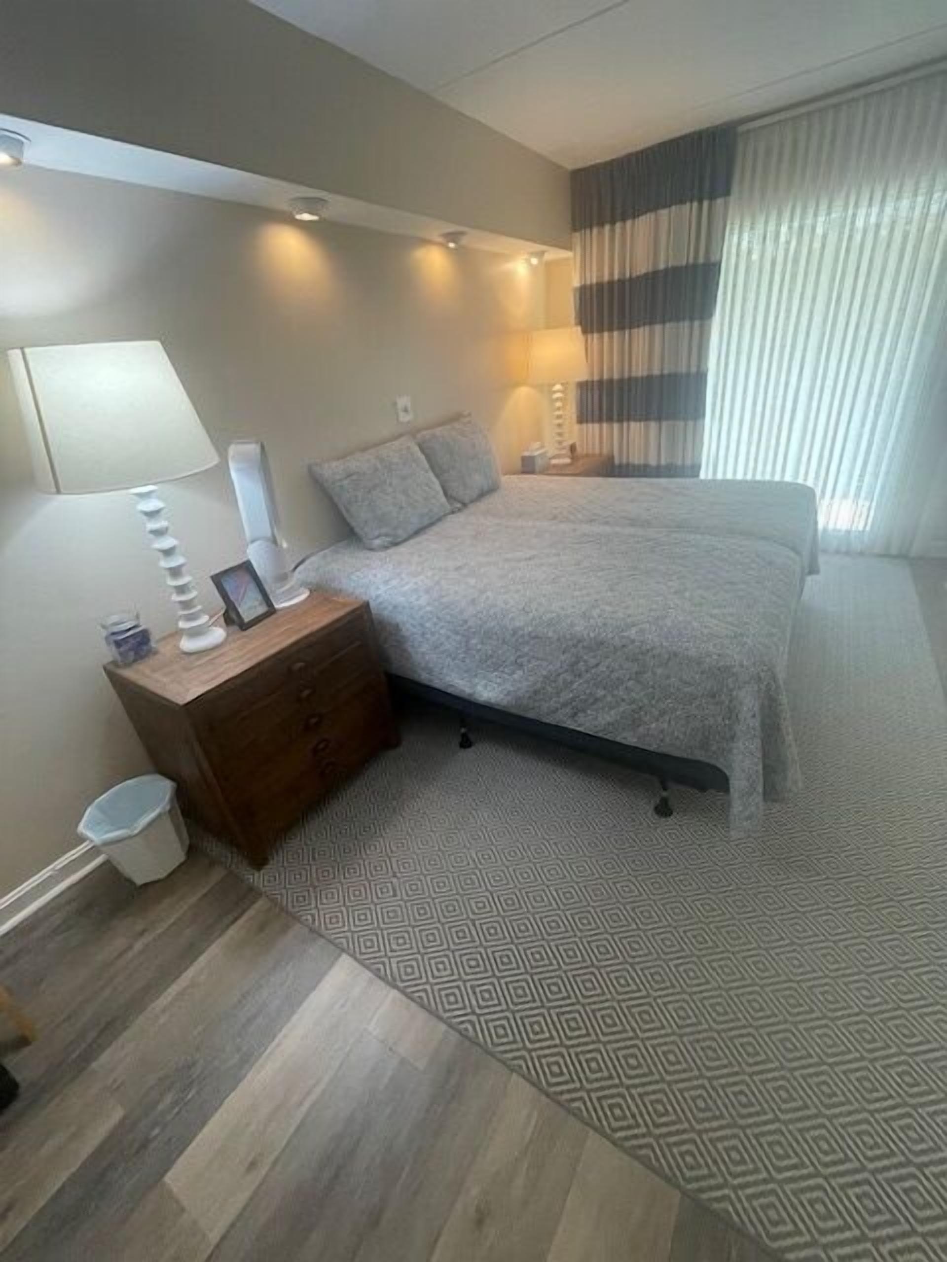 Une chambre à coucher avec un lit, des tables de chevet, une lampe et une poubelle.
