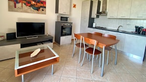 A modern kitchen with a microwave, oven, and sink. There is a dining table with chairs and a flat-screen TV on a stand. - Enjoy House - close to the lake and all amenities (Desenzano del Garda)