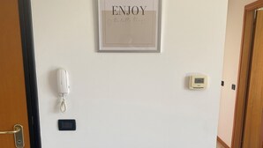 A hallway with a framed sign that reads "ENJOY the little things," a phone, a thermostat, and a bench. - Enjoy House - close to the lake and all amenities (Desenzano del Garda)