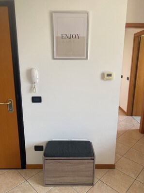 A hallway with a framed sign that reads "ENJOY the little things," a phone, a thermostat, and a bench. - Enjoy House - close to the lake and all amenities (Desenzano del Garda)