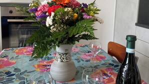A dining table with a floral tablecloth, a vase of flowers, two wine glasses, and a bottle of wine. - Enjoy House - close to the lake and all amenities (Desenzano del Garda)