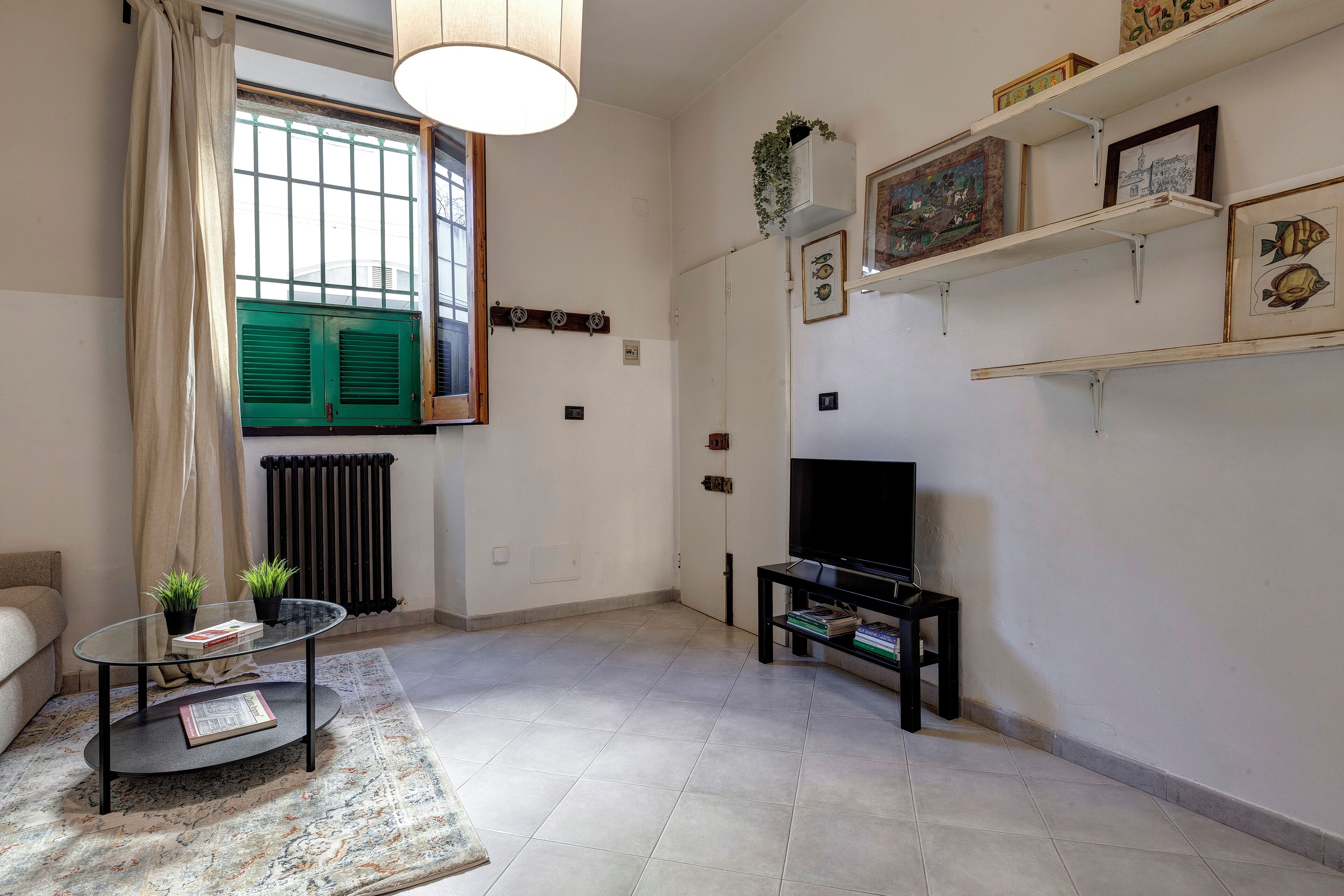 Een woonkamer met een glazen salontafel, een bank, een televisie en een radiator.