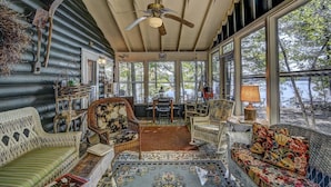 A cozy room with wicker furniture, a ceiling fan, and large windows overlooking a natural landscape. - Stepaway Vacation Rentals - Frog Hollow on Finley Lake (St Germain)