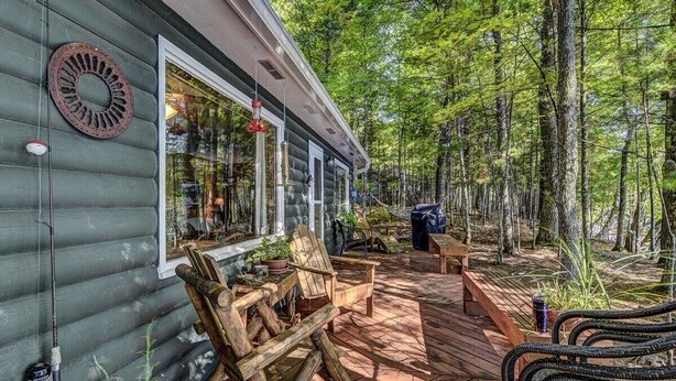 A cabin with a deck, wooden chairs, and a fishing rod. - Stepaway Vacation Rentals - Frog Hollow on Finley Lake (St Germain)