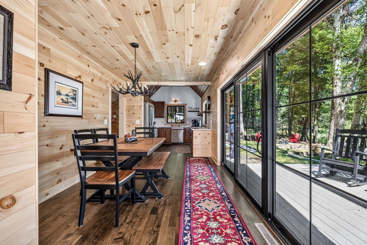 A wooden interior with a dining area, kitchen, and large windows overlooking a deck.