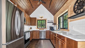 A kitchen with wooden cabinets, a stainless steel refrigerator, a dishwasher, and a window with a view of trees. - An Adventure Awaits -  Stepaway Vacation Rentals (St.Germain)