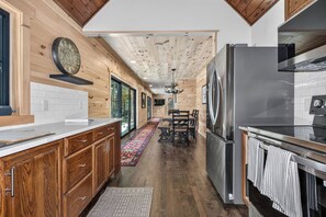 A modern kitchen with wooden walls, a stainless steel refrigerator, and a dining area with a rug. - An Adventure Awaits -  Stepaway Vacation Rentals (St.Germain)