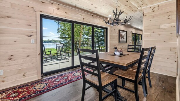 A dining area with a wooden table and chairs, large windows, and a chandelier. - An Adventure Awaits -  Stepaway Vacation Rentals (St.Germain)