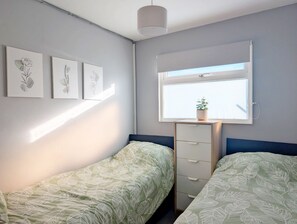 Een slaapkamer met twee enkele bedden, een dressoir, een raam met een plant op de vensterbank en drie aan de muur hangende kunstwerken.