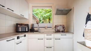Een moderne keuken met witte kasten, een inbouwoven en een raam met uitzicht op groen.