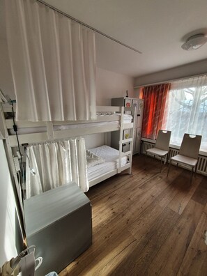 Una habitación con literas, un escritorio, sillas, un radiador y una ventana con cortinas.