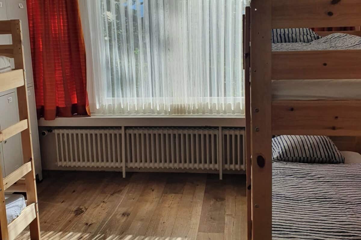 Une chambre avec un lit superposé, un radiateur et une fenêtre avec des rideaux.