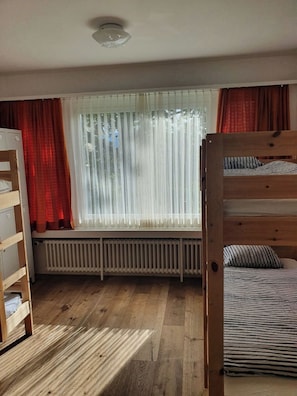 Une chambre avec un lit superposé, un radiateur et une fenêtre avec des rideaux.